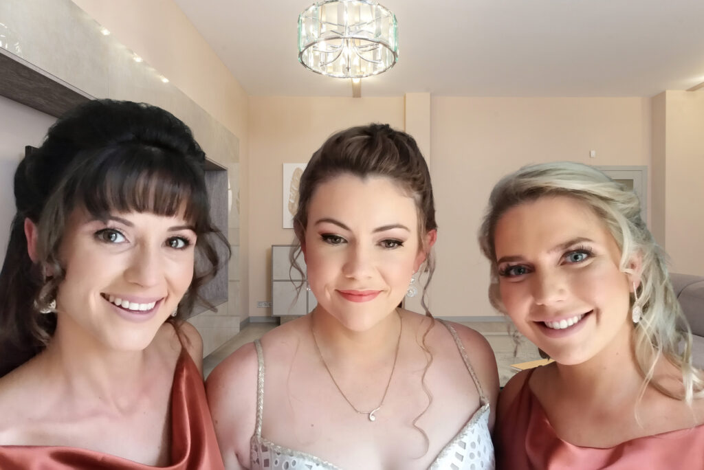Three women smiling together in matching formal attire for a bridal party.