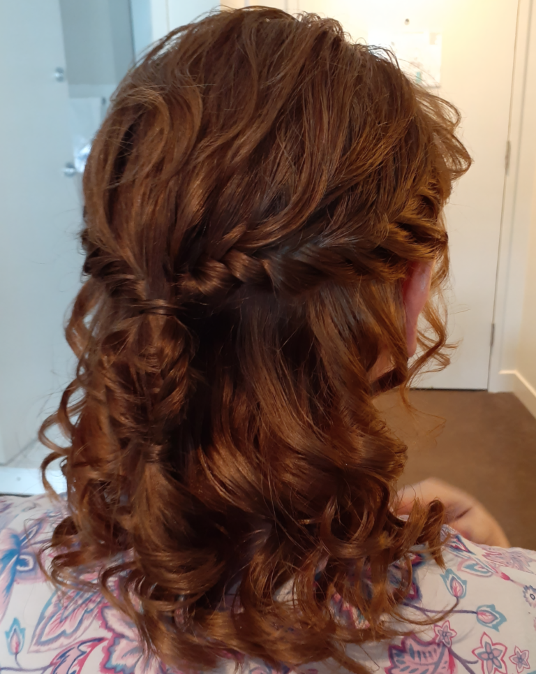 Brunette hair styled in a half-updo with soft curls and a braided crown detail.