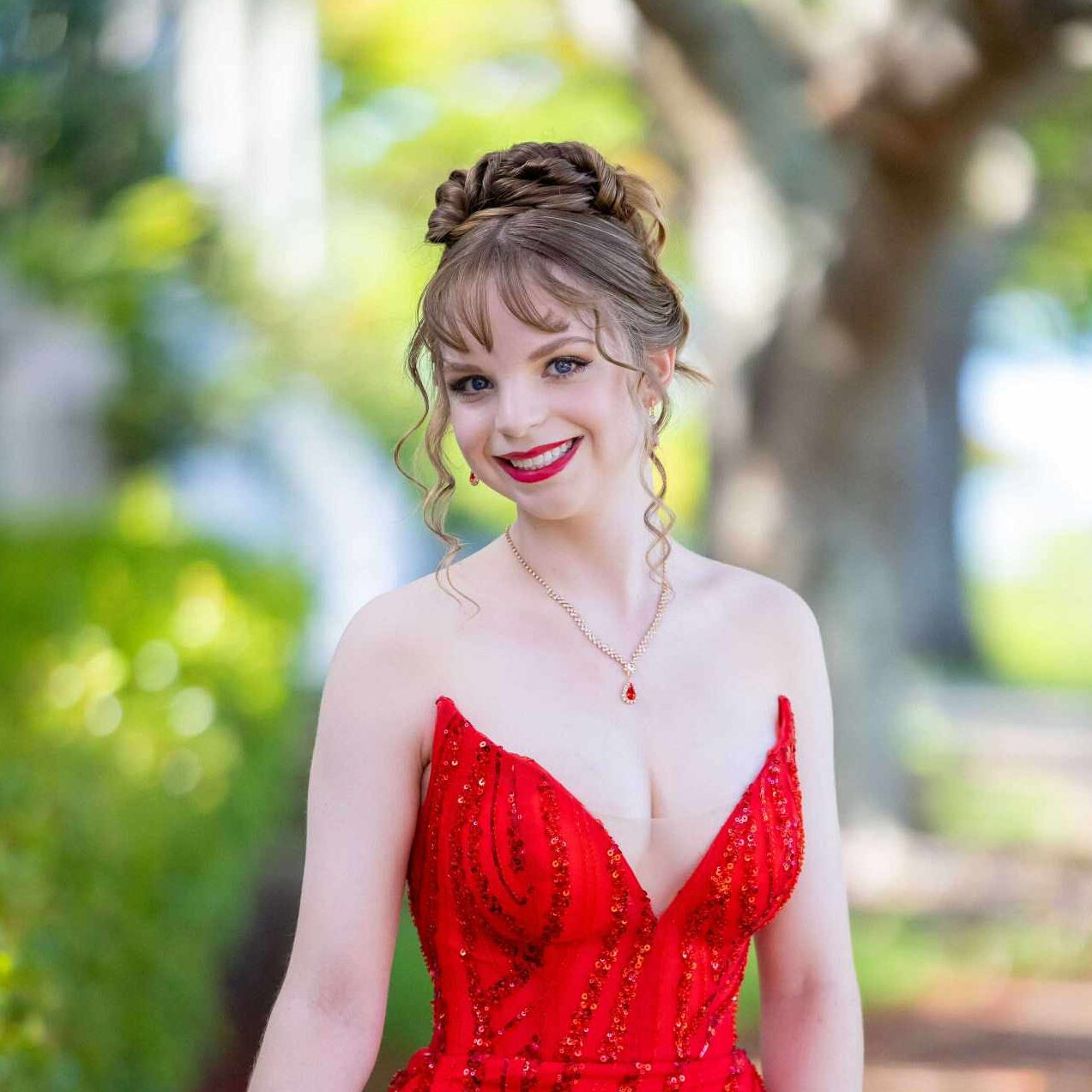 Young woman with an elegant updo hairstyle and red lipstick wearing a sequined red formal dress and a teardrop necklace.