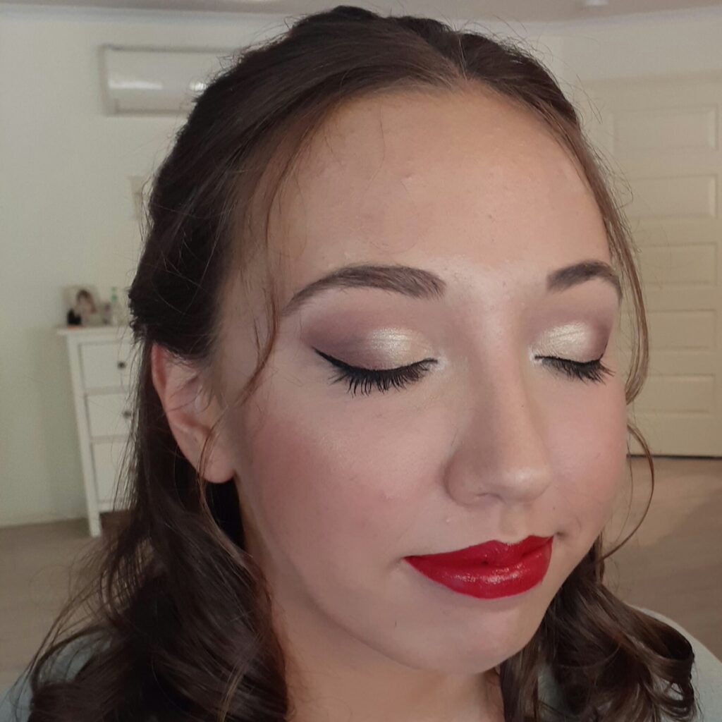 Woman with eyes closed wearing natural eye makeup, winged eyeliner, and bold red lipstick.
