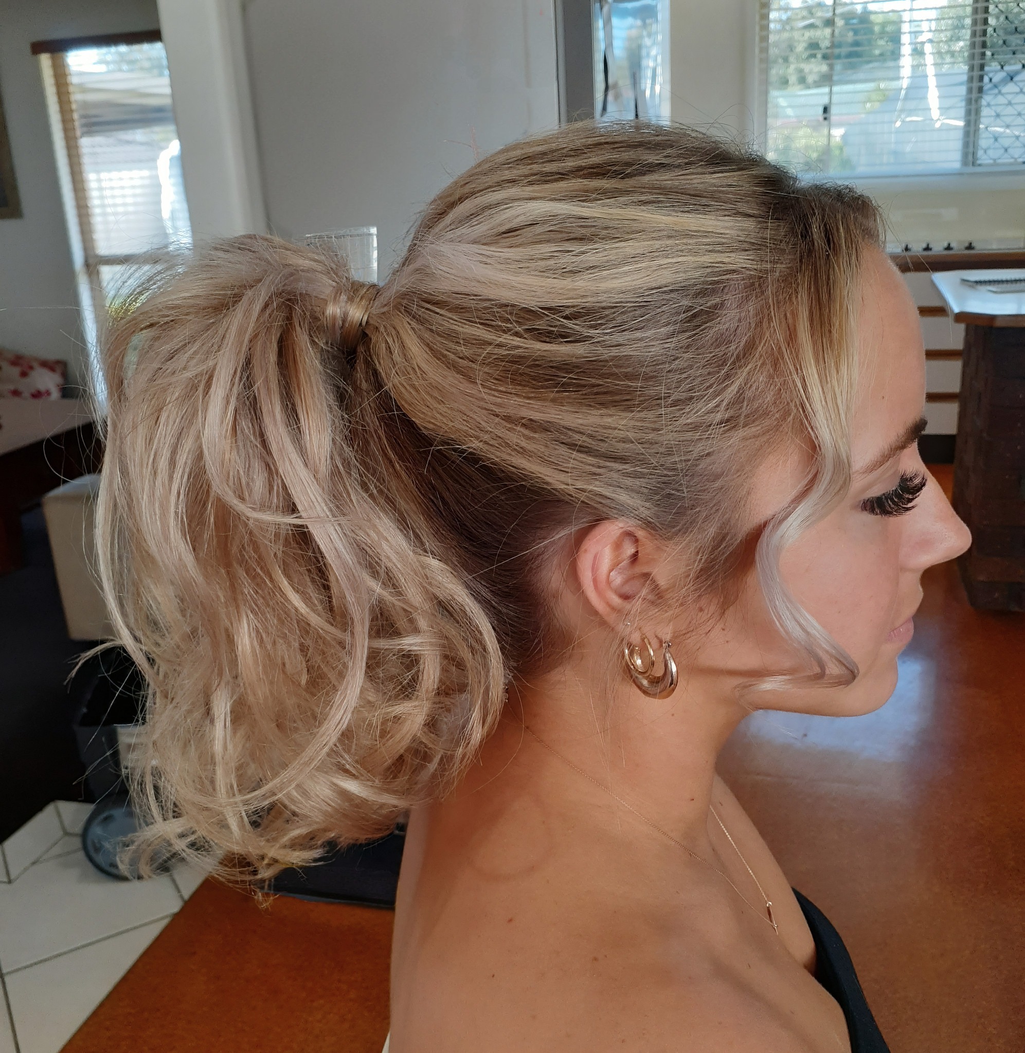 Woman with blonde hair styled in a textured high ponytail with loose strands framing her face.
